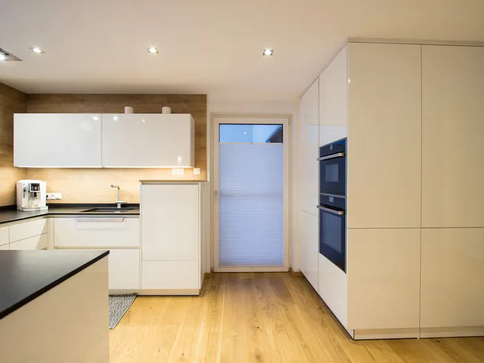 Moderne Einbauküche mit weißen Hochglanzfronten, Holzfußboden und integrierten Geräten