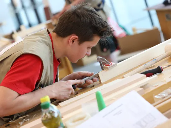 Junger Handwerker arbeitet konzentriert mit einem Stechbeitel an einem Holzstück in der Werkstatt