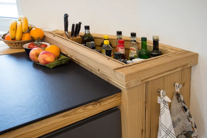 Küchentheke mit Obstschale, Gewürzen, Messern und Flaschen in einem Holzregal
