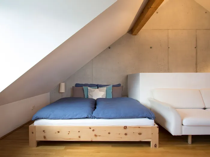 Modernes Schlafzimmer im Dachgeschoss mit Holzbett, blauer Bettwäsche und weißem Sofa