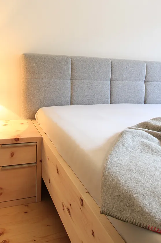 Modernes Schlafzimmer mit Holznachttisch, grauem Polsterbett und gefalteter Wolldecke