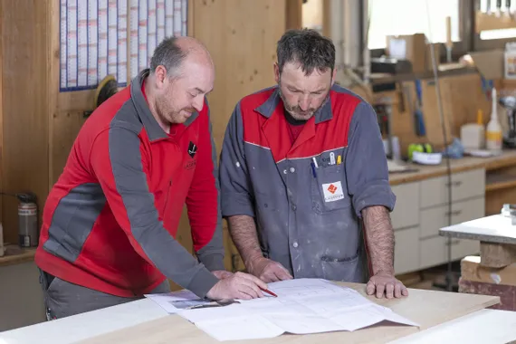 Zwei Handwerker besprechen Baupläne in einer Holzwerkstatt