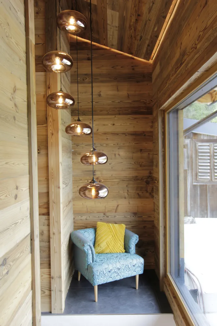 Gemütliche Leseecke mit blauem Sessel, gelbem Kissen und Hängelampen im Holzinterieur