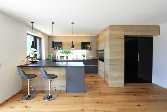 Moderne offene Küche mit Holzfronten, schwarzer Arbeitsplatte und Hängelampen