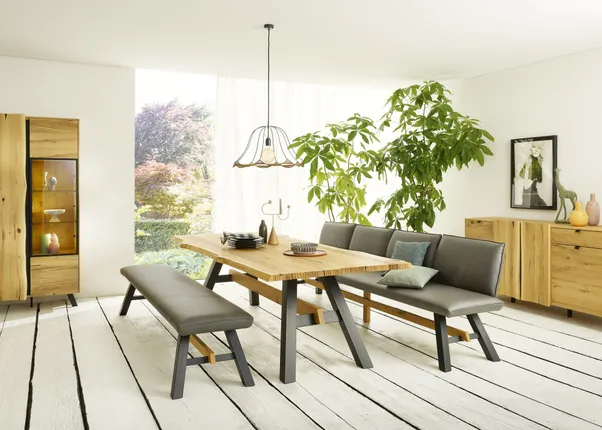 Modernes Esszimmer mit Holzmöbeln, grauen Sitzbänken und viel Tageslicht