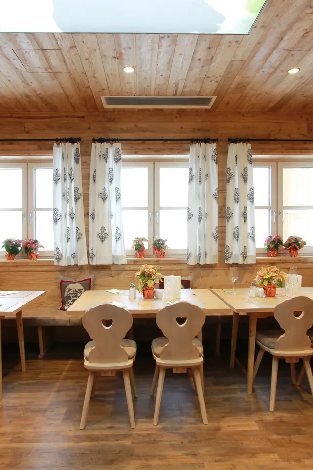 Gemütliches Restaurant mit Holzwänden, dekorierten Tischen und weißen Vorhängen im Alpenstil