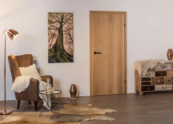 Gemütliches Wohnzimmer mit Sessel, Stehlampe, Holztür, Naturbild und Vintage-Kommode auf Holzfußboden