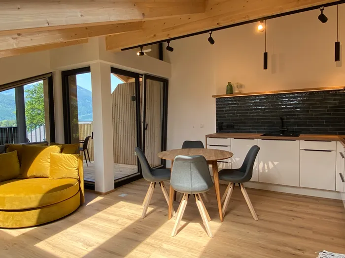 Moderne Ferienwohnung mit offener Küche, Esstisch und gelbem Sofa mit Bergblick