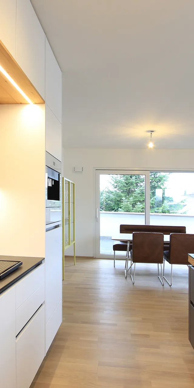 Moderne offene Wohnküche mit Holzfronten, Kochinsel und Essbereich mit Lederstühlen