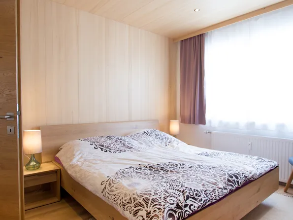 Modernes Schlafzimmer mit Holzbett, gemustertem Bettbezug und natürlichem Licht durch ein Fenster