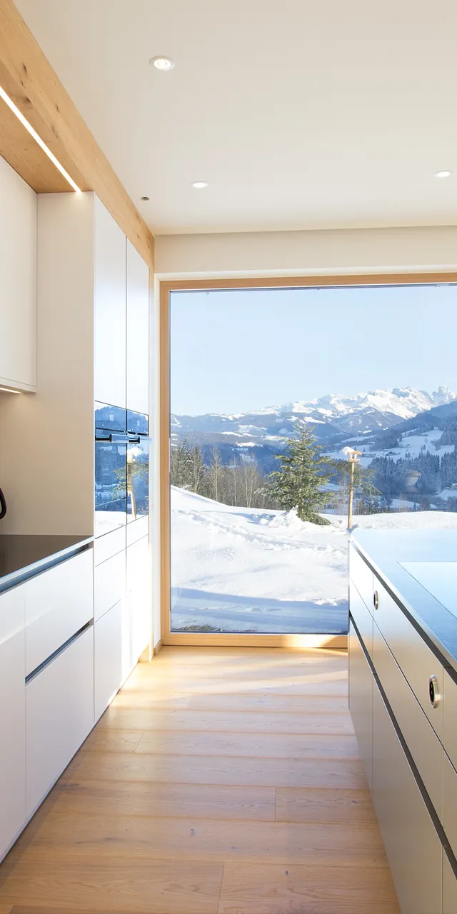 Moderne weiße Küche mit Bergblick durch große Fenster und minimalistischer Einrichtung