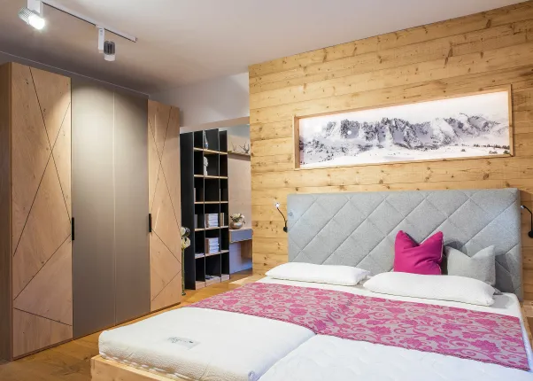 Modernes Schlafzimmer mit Holzwand, grauem Polsterbett und pinker Tagesdecke