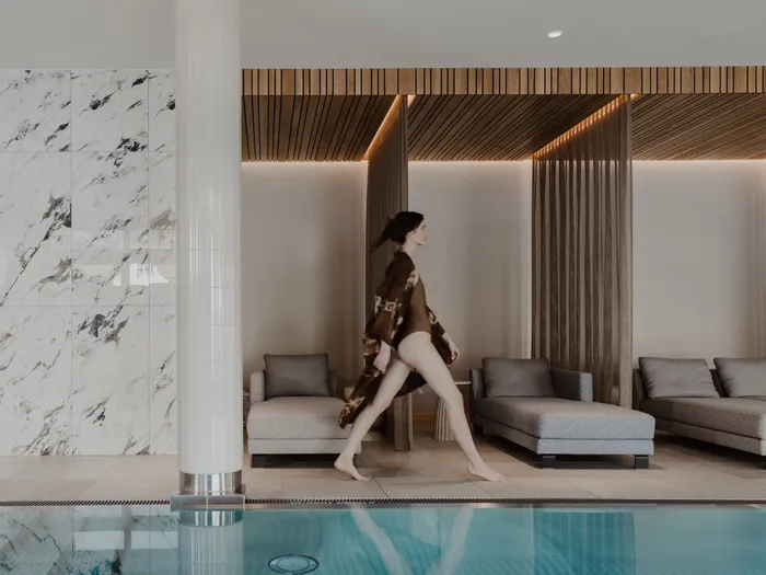 Frau im Badeanzug geht an Liegen und indoor Wellnesspool vorbei