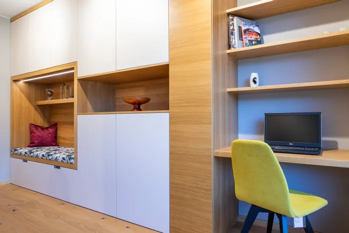 Moderner Arbeitsbereich mit Einbauschränken, Regalwand, Laptop und gelbem Stuhl neben Sitznische