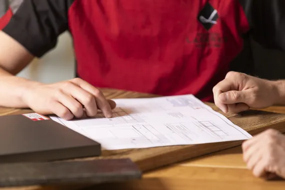 Zwei Personen besprechen technische Zeichnung auf Holzschreibtisch