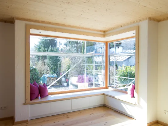 Helles Wohnzimmer mit Eckfenster, Holzverkleidung und Sitzbank mit pinken Kissen