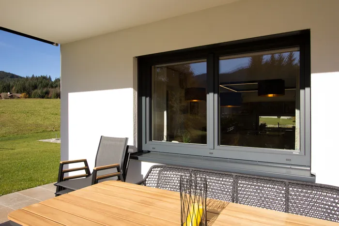 Moderne Terrasse mit Holztisch, Gartenstühlen und Blick auf Wiese und Wald