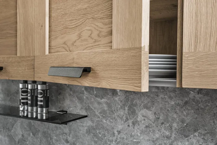 Offener Küchenschrank mit weißen Tellern und Holzfront über grauer Steinwand