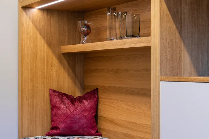 Gemütliche Sitznische mit floralem Polster, rotem Kissen und Holzregal mit Gläsern