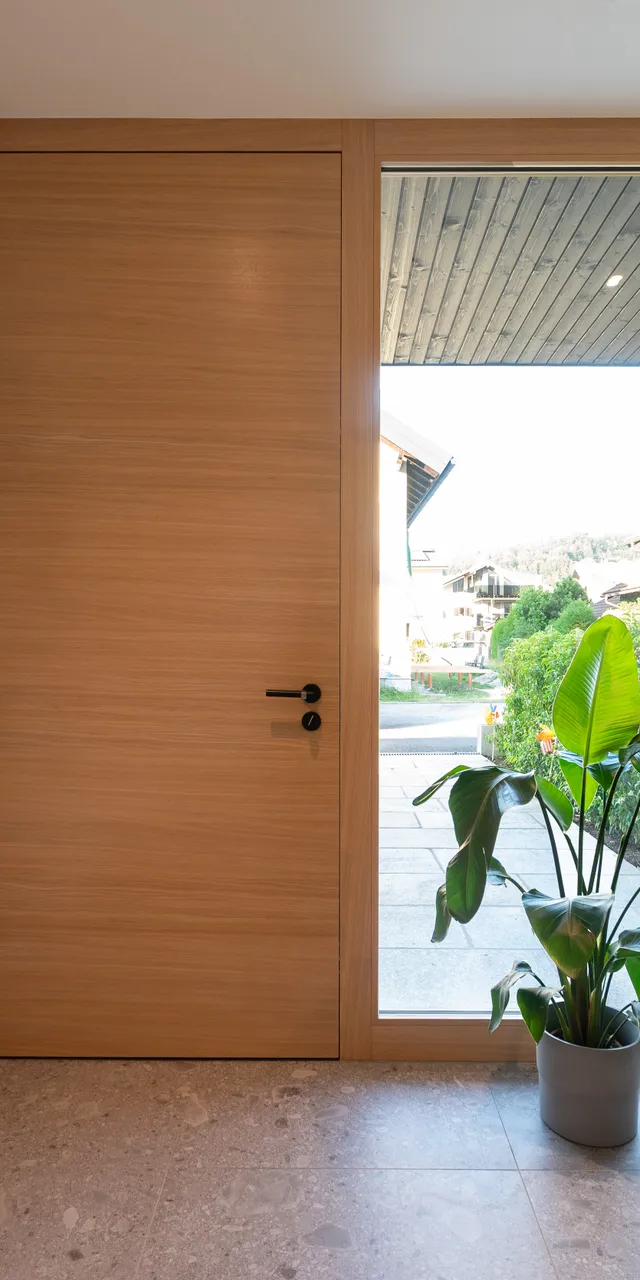 Moderne Diele mit Holz-Eingangstür, großem Fenster, Zimmerpflanze und Sessel