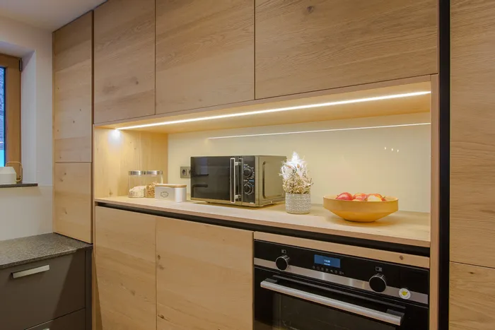 Moderne Küche mit Holzfronten, Mikrowelle, LED-Beleuchtung und Schale mit Äpfeln