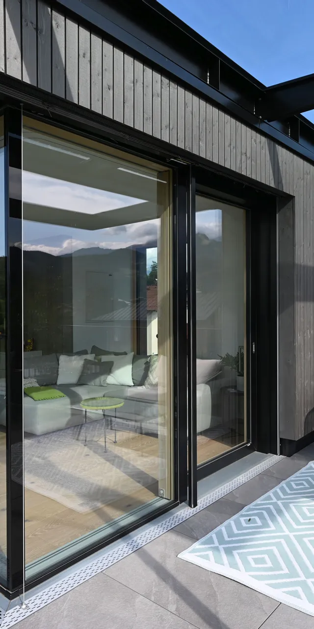 Moderne Terrasse mit Glasüberdachung, gemütlichen Sitzmöbeln und Panoramablick auf die Berge