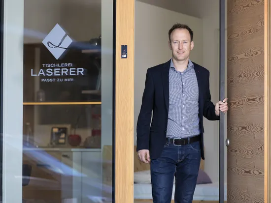 Mann öffnet Holztür eines modernen Büros mit Logo der Tischlerei Laserer