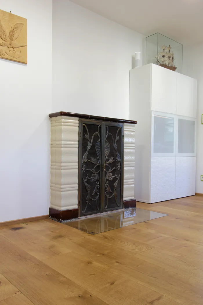 Verzierter Jugendstil-Kamin mit schwarzer Gusstür in modernem Wohnzimmer mit Holzfußboden