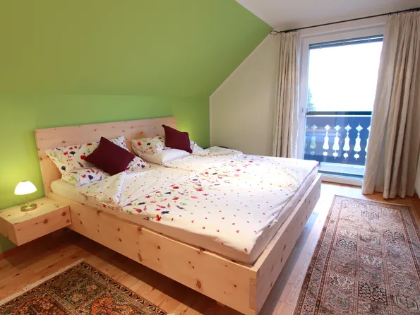 Helles Schlafzimmer mit Doppelbett aus Holz, Bettwäsche mit Blumenmuster und Zugang zum Balkon