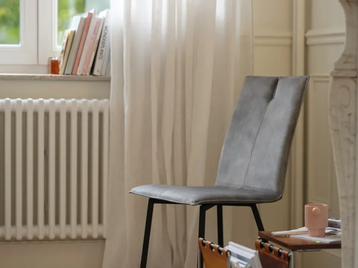 Moderner grauer Stuhl neben Beistelltisch mit Zeitschriftenhalter in hellem Wohnzimmer