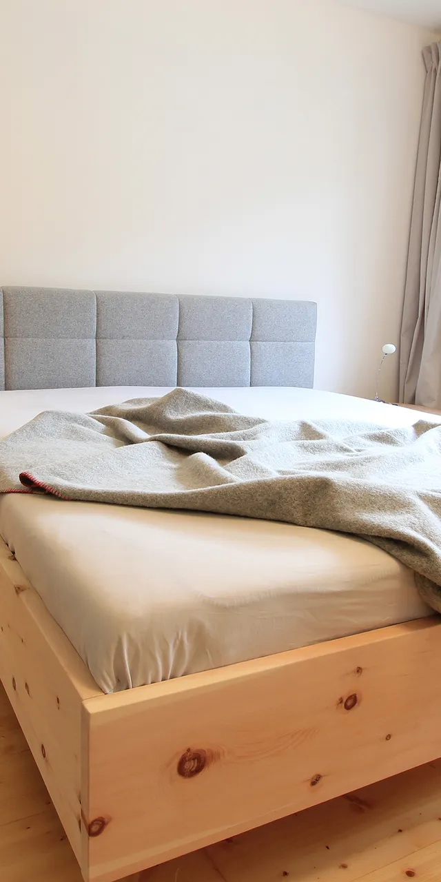 Modernes Schlafzimmer mit Holzbett, grauem Kopfteil, Nachttischlampe und Vorhängen am Fenster