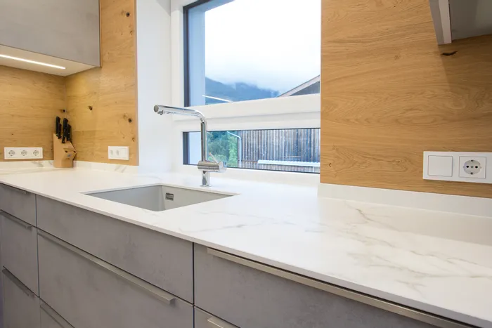 Moderne Küche mit weißer Marmorarbeitsplatte, Edelstahlspüle und Holzverkleidung
