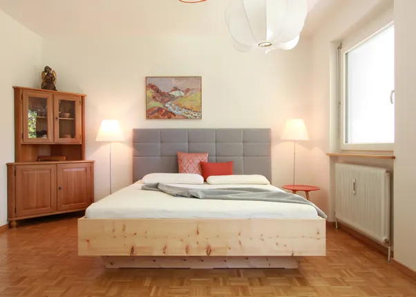 Modernes Schlafzimmer mit grauem Polsterbett, Holzmöbeln und dezenter Beleuchtung