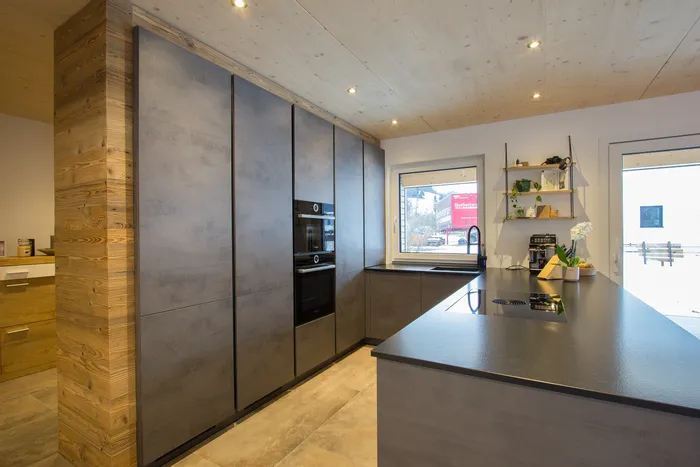 Moderne Einbauküche mit Betonoptik, Kochinsel und Holzakzenten unter Holzdecke