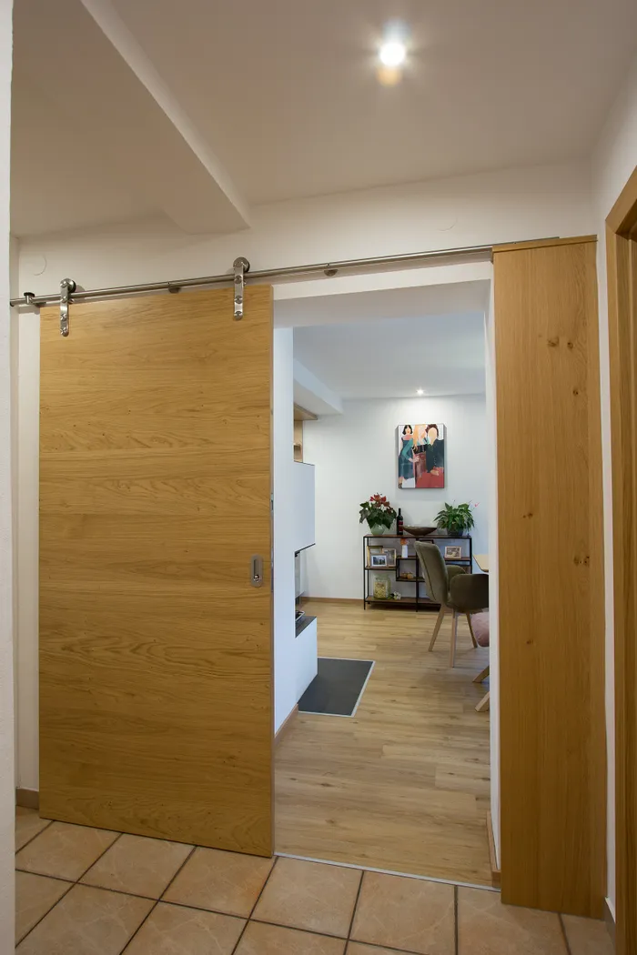 Offene Schiebetür aus Holz mit Blick in ein modern eingerichtetes Wohnzimmer mit Parkettboden