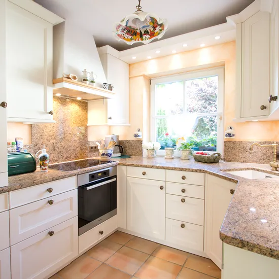 Helle Landhausküche mit Granit-Arbeitsplatten, weißen Schränken und Blick auf Garten durch Fenster