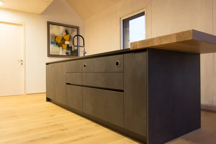 Moderne Kücheninsel mit dunkler Front, Holzarbeitsplatte und Wasserhahn in hellem Innenraum