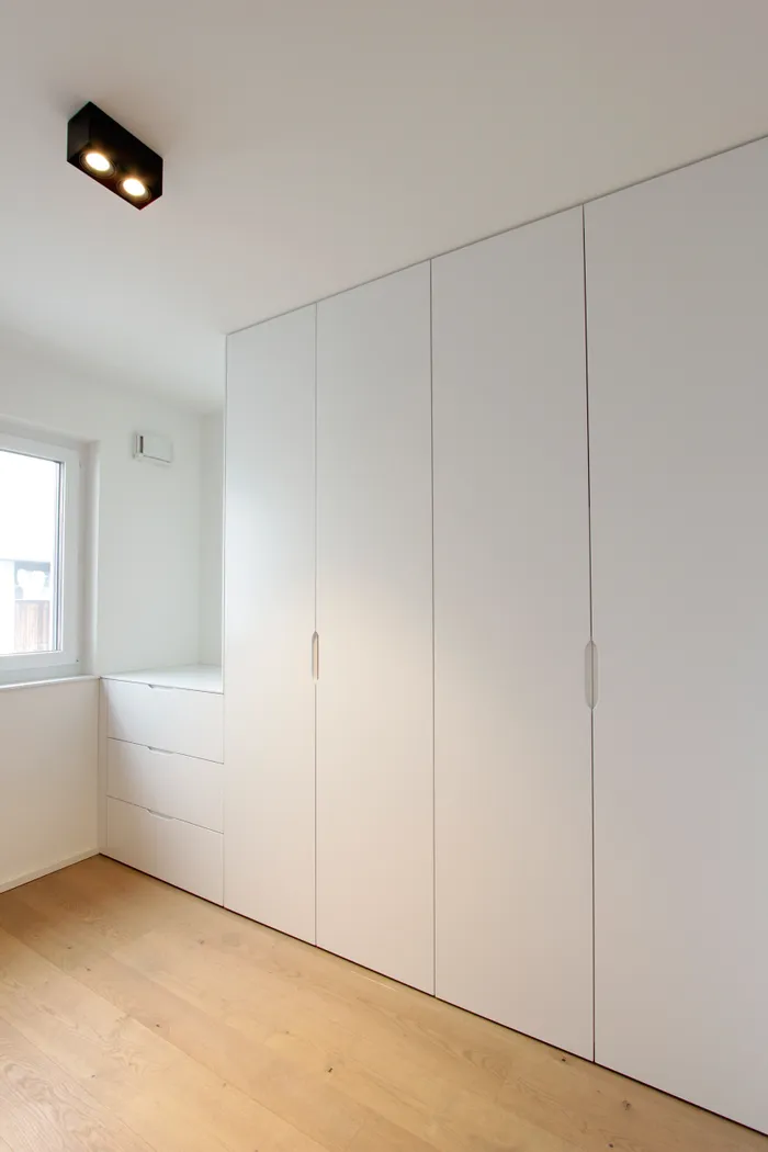 Minimalistischer weißer Einbauschrank mit Schubladen und Kleiderschrank in modernem Schlafzimmer