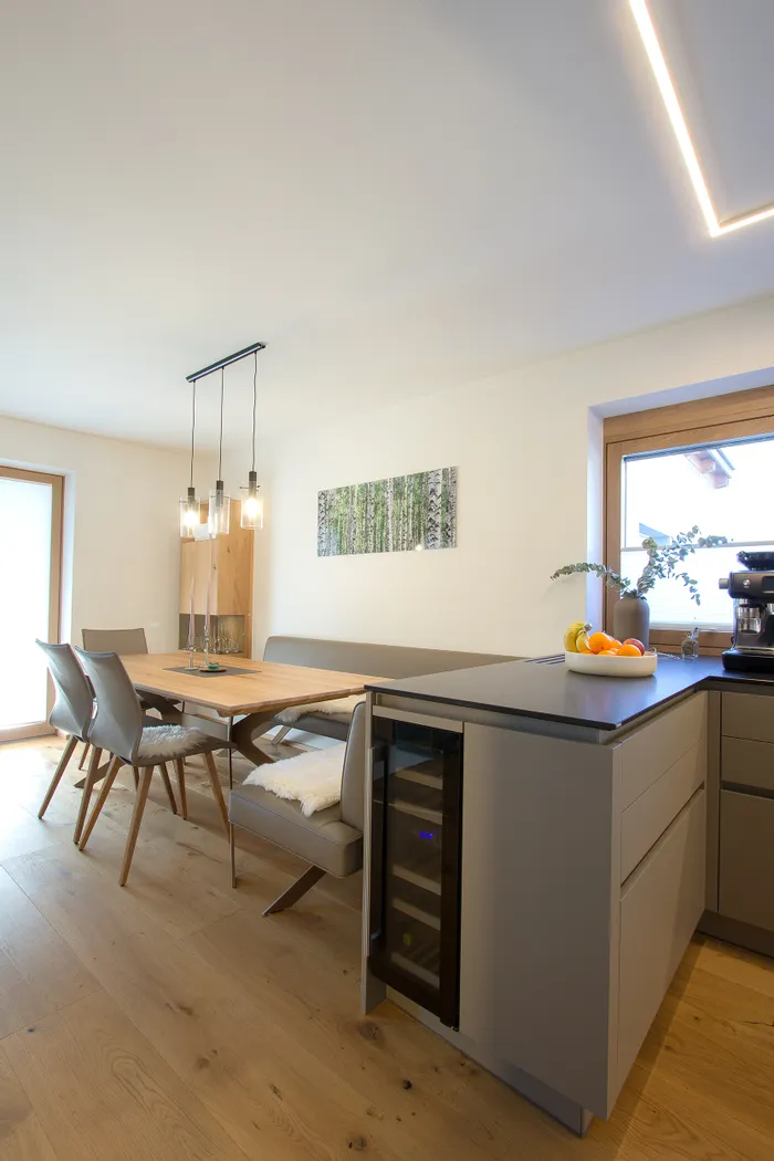 Moderne Essküche mit Holztisch, grauen Stühlen, Hängelampen und Obstschale auf Kücheninsel