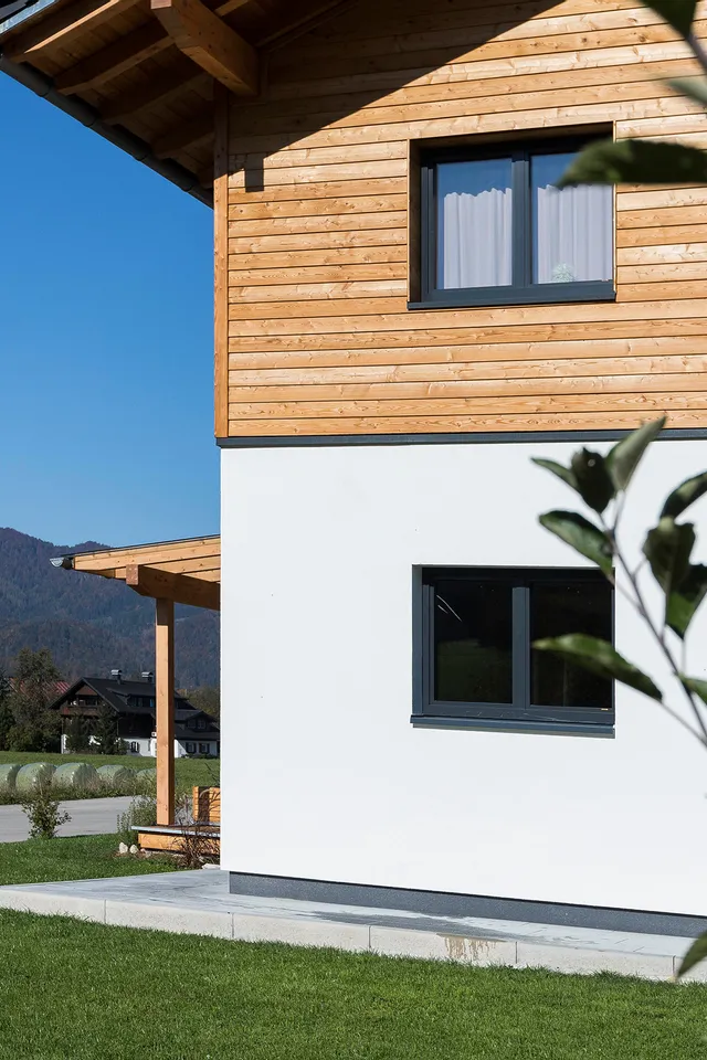 Modernes Holzhaus am Stadtrand mit Alpenblick und grüner Wiese im Vordergrund