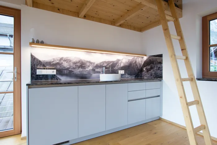 Moderne Küchenzeile mit Alpen-Panoramabild als Rückwand und hellen Holzdetails