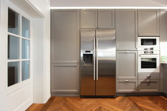 Moderne Einbauküche mit grauen Schränken, Edelstahlkühlschrank und Einbaugeräten auf Fischgrätparkett