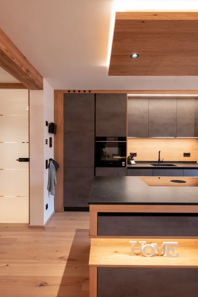 Moderne offene Küche mit Holzdetails, dunklen Fronten und Kücheninsel mit HOME-Dekoration