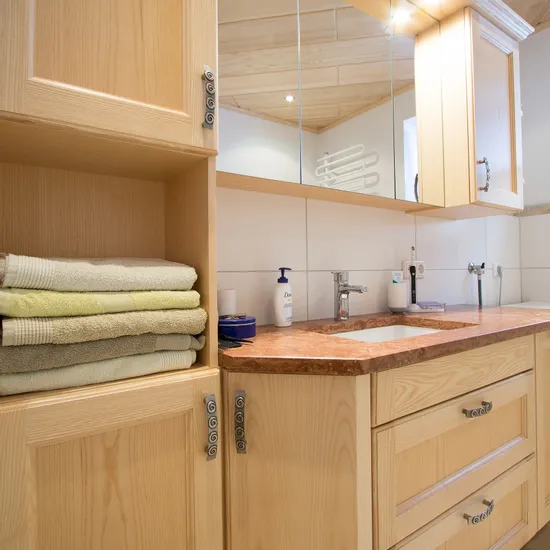 Modernes Badezimmer mit hellen Holzschränken, gefalteten Handtüchern und Waschbecken mit Spiegel