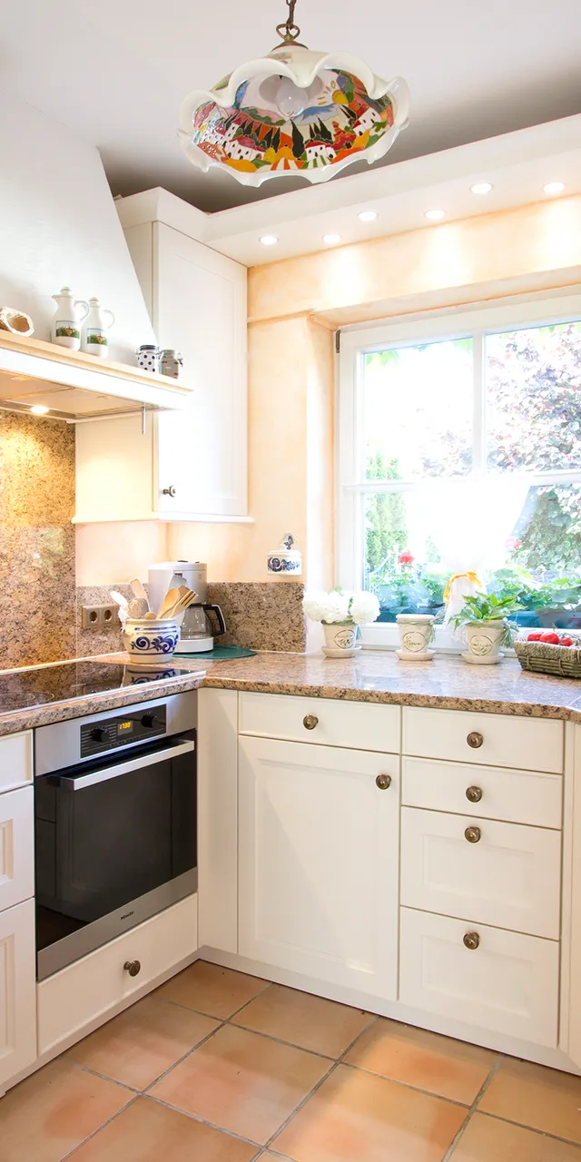 Landhausküche klasisch mit Granit-Arbeitsplatten, weißen Schränken und Blick auf Garten durch Fenster