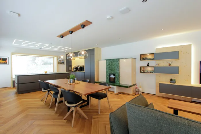 Moderne offene Wohnküche mit Holzboden, Esstisch, Designlampen und Kachelofen
