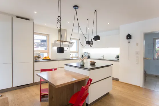 Moderne weiße Einbauküche mit Kücheninsel, Holzdetails und roten Stühlen auf Holzboden