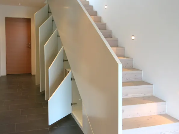 Moderne Holztreppe mit integrierten Staufächern unter jeder Stufe in einem minimalistischen Flur