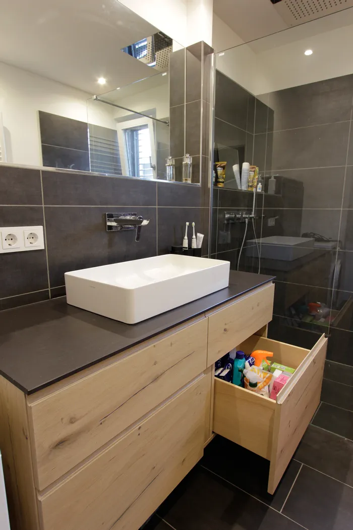 Modernes Badezimmer mit Holzwaschtisch, Aufsatzwaschbecken und offener Schublade mit Reinigungsprodukten