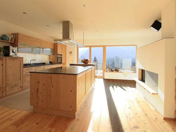 Helle moderne Wohnküche mit Holzverkleidung, Kochinsel und Panoramafenster mit Bergblick